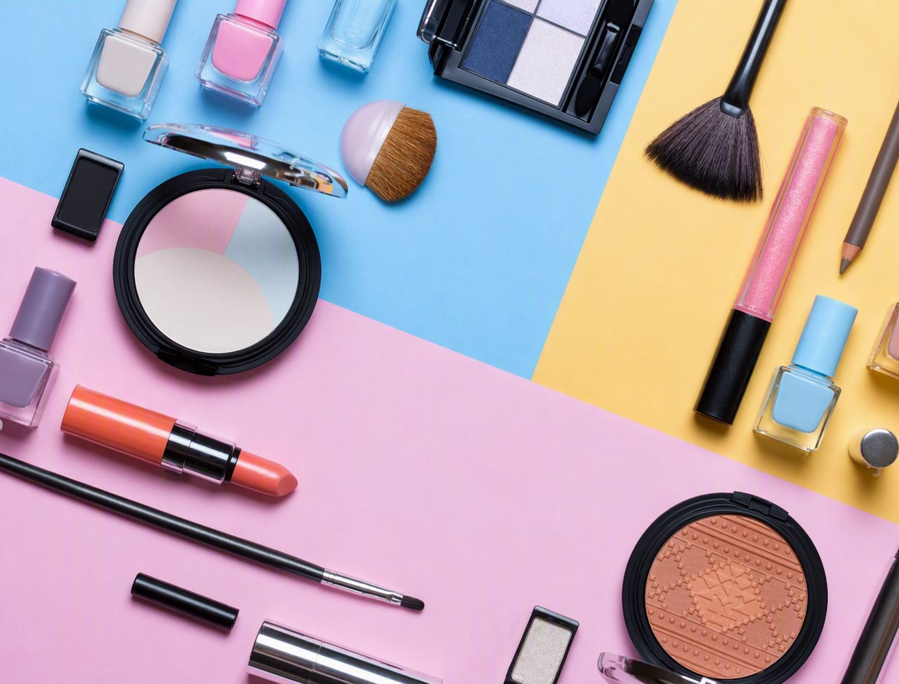 Complete makeup collection flat-lay: eyeshadow palettes, lipsticks, mascara, brushes and nail polish on tri-color background
